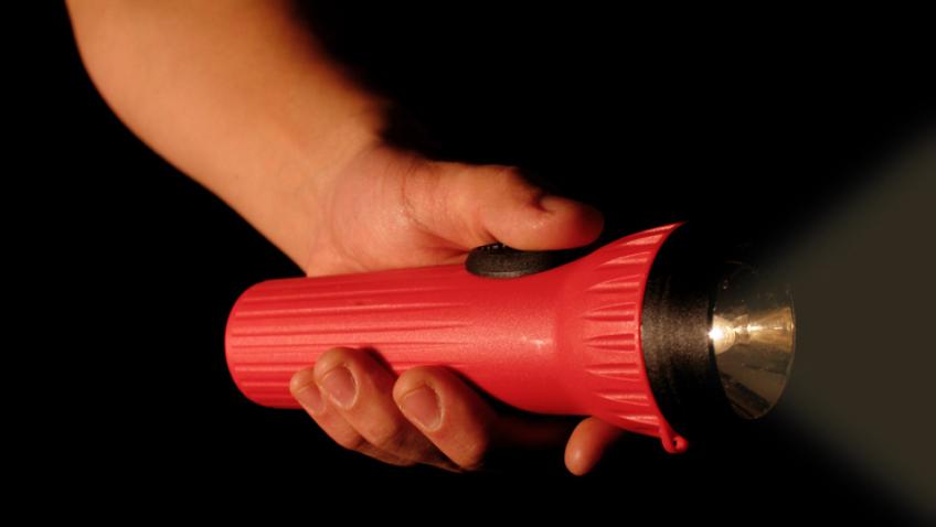 A child’s hand holding a red flashlight in the darkness