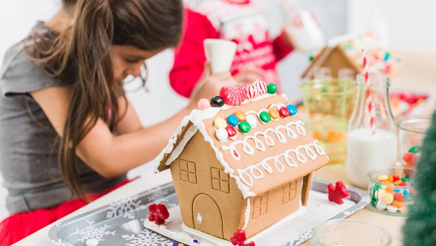  A child  bends over a gingerbread house they are decorating at their kitchen table