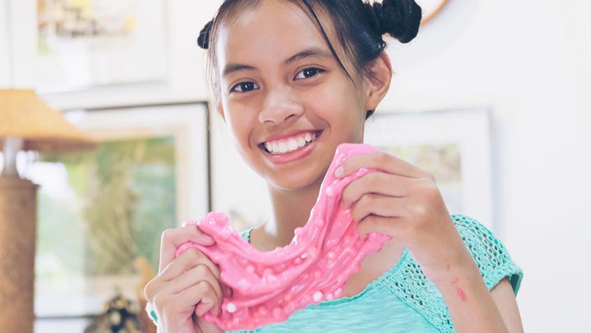 A smiling child holds up bright pink slime with small white spheres mixed into it