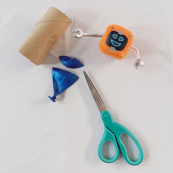 A short cardboard tube, a pair of scissors and a blue balloon with its round top cut off and placed to the side