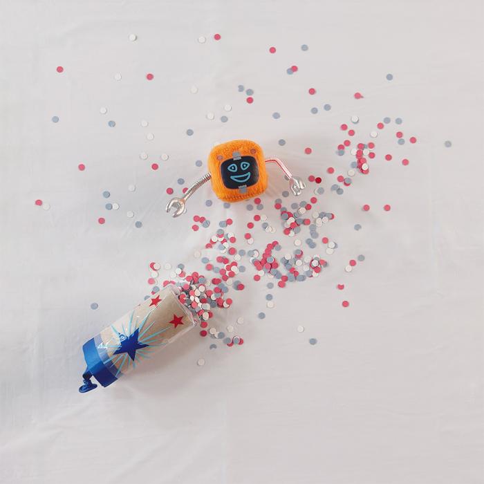 A cardboard tube with the knotted bottom of a balloon stretched over one end on top of a pile of colorful paper circles