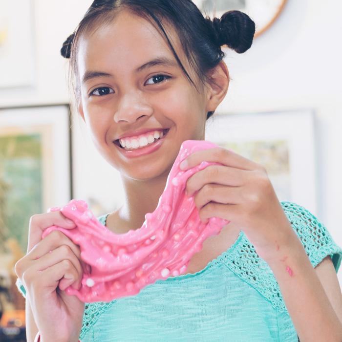 A child smiles and holds up bright pink slime with small balls mixed inside it