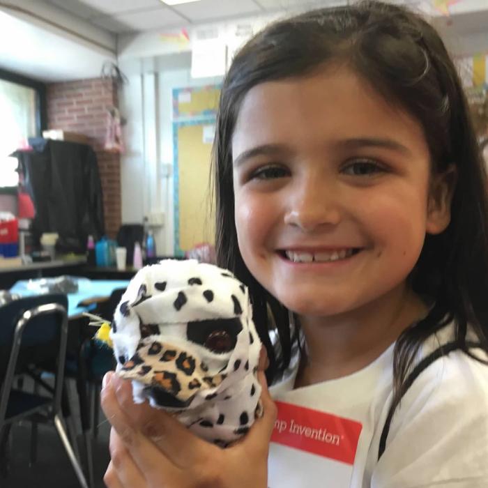 Delaney DeMarco as a young child holds up a robotic dog decorated in tape covered with animal spots