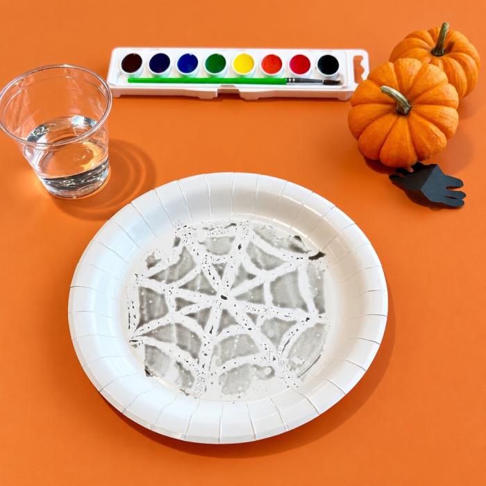 A paper plate with a crayon resist spider web on it revealed with black watercolor paint