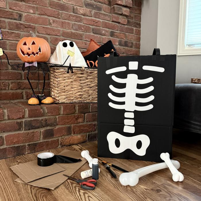 A cardboard box painted in black and white to look like an x-ray beside craft materials and a basket of Halloween decorations