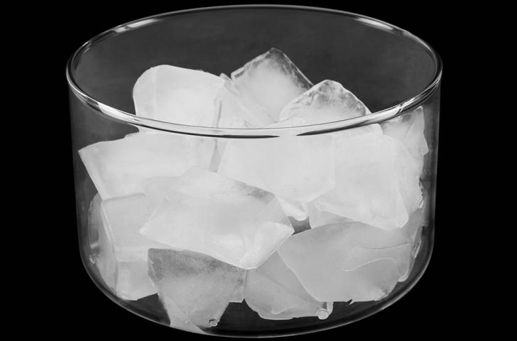 A clear glass bowl filled with ice cubes in front of a black background