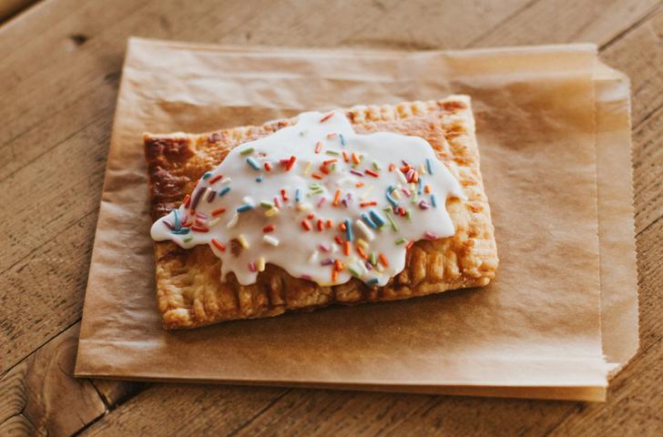 A homemade toaster pastry topped with frosting and sprinkles rests on top of a small wax paper bag