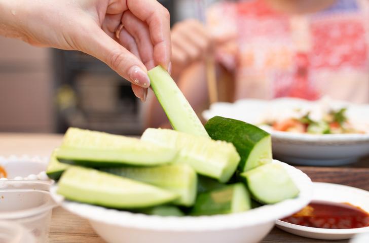 A hand lifts a pickle slice from a plate piled high with pickles