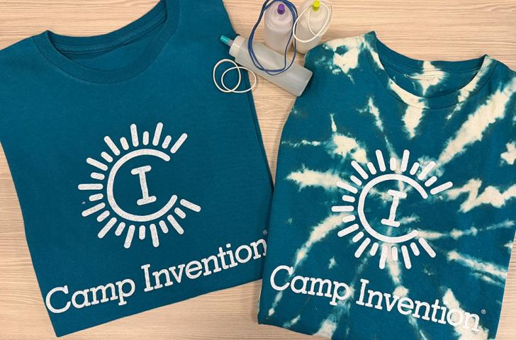 Two dark blue Camp Invention shirts with one shirt having been reverse tie dyed and small squeeze bottles between them