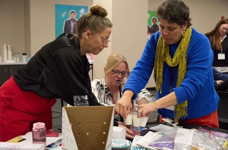 A trio of educators work together to assemble an invention prototype using craft materials