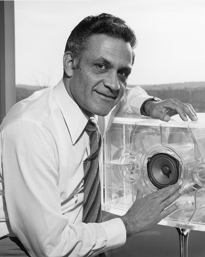 Amar Bose poses next to a large plexiglass speaker