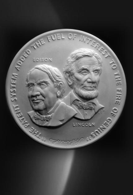 A medal featuring Thomas Edison and Abraham Lincoln with the quote “the patent system added the fuel of interest to the fire of genius”