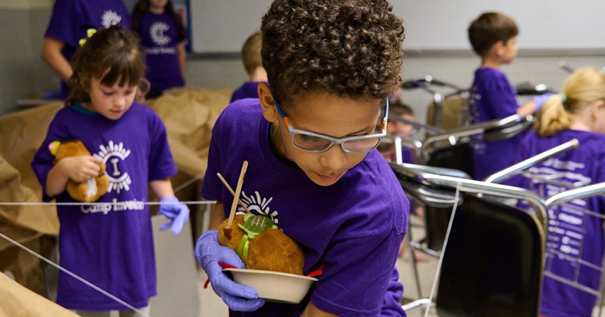 A Camp Invention camper leans forward to collect forensic evidence while holding their robotic capybara sidekick