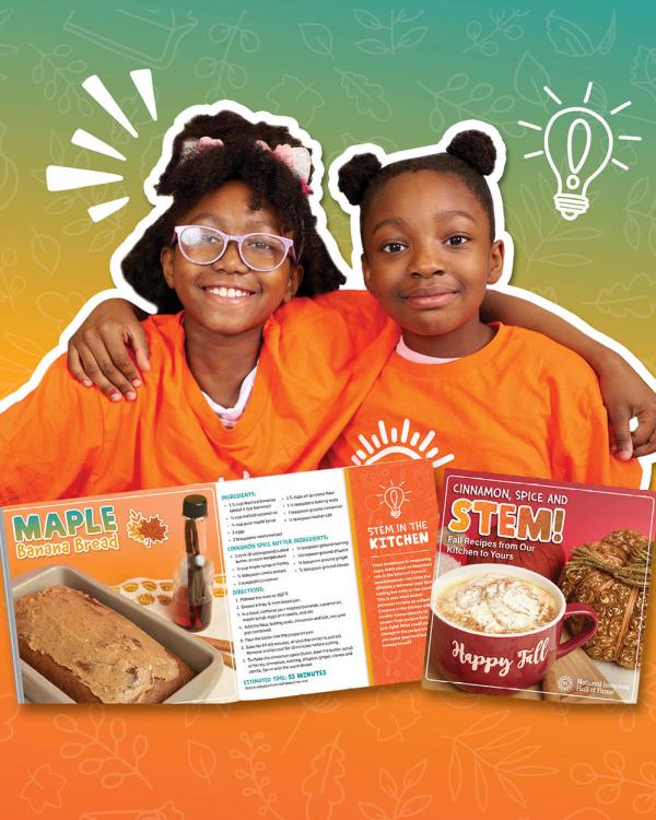 Two children wearing matching orange shirts smile behind a recipe book of fall-themed dishes