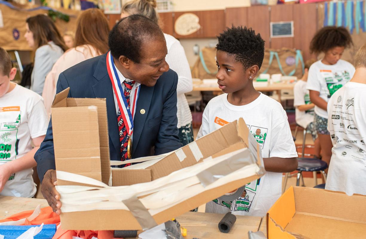 Inductee Victor Lawrence listens as a Camp Invention camper describes the structure they built using cardboard
