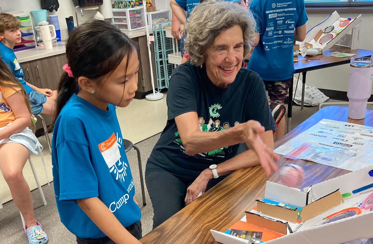 Frances Ligler smiles and tosses a small foam ball up a cardboard ramp as an elementary student looks on