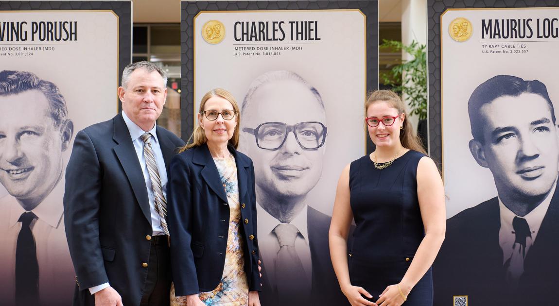 A trio of people smile in front of a museum exhibit panel featuring Charles Thiel